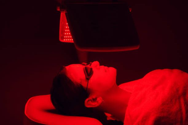 Young woman having red LED light facial therapy treatment in beauty salon. Beauty and wellness concept